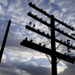 Ritzville WA 25 Silhouette of a tall utility pole with multiple crossbars and glass insulators stands against a cloudy Ritzville, WA sky, with late afternoon or early evening light glowing in the background.