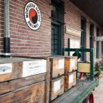 Ritzville WA 23 A vintage wooden cart loaded with wooden crates sits on a brick platform outside the historic Northern Pacific Railway station in Ritzville, WA, with brick walls, old signage, and a timetable visible in the background.