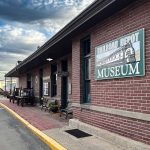 Ritzville WA 30 A brick building in Ritzville, WA, with a large sign reading "Railroad Depot Museum," wooden benches, and historical display pieces outside; the scene is under a partly cloudy sky at this small-town train depot.