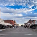 Ritzville WA 16 A view down a wide, empty main street in Ritzville, WA, lined with historic brick and wooden storefronts under a blue sky with scattered clouds.