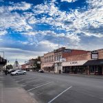 Ritzville WA 13 A quiet Ritzville, WA small-town street with parked cars, brick shopfronts, and a “Drugs” sign under a blue sky with scattered clouds. The empty sidewalks add to the peaceful and calm atmosphere.
