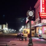 Ritzville WA 14 A small town street at night in Ritzville, WA features a vintage clock on a corner, neon lights from a sports center, parked cars, and glowing shop windows, creating a quiet, nostalgic atmosphere.