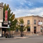 Ritzville WA 10 A small-town street corner in Ritzville, WA, with a brick building, a bar and grill featuring a retro Pastime Sports Center sign, a bank, a street clock, and trees under a partly cloudy sky.