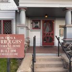 Ritzville WA 32 A sign in front of a historic Ritzville, WA house reads “Dr. Frank R. Burroughs’ Historical Home. Built 1890. Remodeled 1902.” The home features gray columns, a red door, plaques, and steps leading to the entrance.