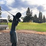 Ritzville WA 42 A metal statue of a golfer in mid-swing stands on mulch near a green lawn and trees in Ritzville, WA, with a partly cloudy sky overhead.