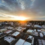 Ritzville WA 17 Aerial view of Ritzville, WA at sunset, with sunlight streaming through clouds, illuminating streets, buildings, and silos, while fields stretch out in the background.